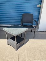 Full view of the patio chair and glass top side table in front of a blue garage door.