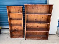 Photo showing two wooden shelves with medium-brown finish placed side by side against a blue storage shutter.