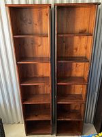 Photo showing two tall wooden bookshelves side by side, each with six shelves, medium brown finish, normal wear and dust visible.