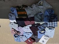 Lot of 16 men's shirts in various styles and colors laid out on ground with visible size and brand tags.