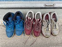 Lot of three pairs of used Nike shoes: blue high-tops, maroon low-tops, white low-tops with gold design.