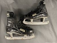 Side view of two black leather Bauer Black Panther men's hockey skates showing the left and right skate, highlighting the logo patches and skate condition.
