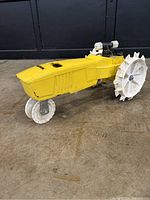 Side angle of yellow Nelson Rain Tractor traveling lawn sprinkler showing white spiked iron rear wheels and front caster wheel, on indoor concrete floor.