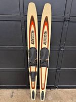 Front top view of the pair of vintage Connelly Flex 250 water skis showing beige wood finish with orange and black graphics and black bindings.