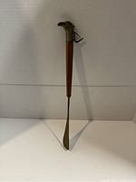 Front view of the full shoehorn showing brass horseshoe head and wooden handle with metal blade.