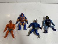 Top view front of four He-Man action figures showing front details and colors