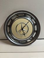 Front view of the Mercedes Benz hub cap clock showing the star emblem and clock hands on a beige center.
