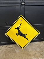Yellow diamond-shaped metal deer crossing sign with black silhouette, showing visible wear and holes for mounting.