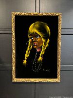 Framed black velvet portrait painting of a blonde girl with two braids and blue eyes with tears, signed '74, hanging on dark wall.