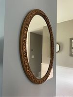 Side angle view of the oval gold gild mirror showing depth and ornamental floral frame detail.