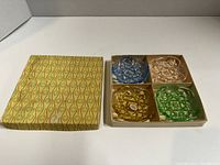 Top view image showing all four colored glass dishes in original box with patterned lid to the side.