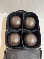 Four vintage Henselite lawn bowling balls placed in a black carrying case with divided sections.