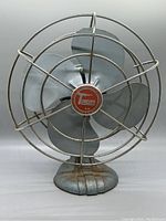 Front view of vintage Torcan desk fan showing four metal blades, central logo, and wire cage.