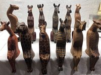Front view displaying 12 carved wooden animal figurines including giraffes, zebras, and an elephant. Various height and painted details visible.