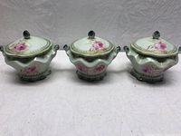 All three Nippon porcelain lidded vessels displayed front-facing showing floral designs and gold accents