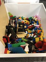 Wide view of white bin filled with assorted Lego bricks and pieces in various colors and shapes, including specialty black wing elements and frame structure.
