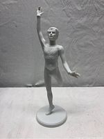 Front view of an unpainted white bisque porcelain male dancer figurine standing on one leg with one arm raised.