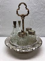 Front view of the complete HUGO silver plated cruet set showing tray, handle, and all four glass containers with stoppers and shaker tops