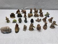 Wide view of 27 mini ceramic figurines arranged on white surface, showing variety of animal and character shapes.