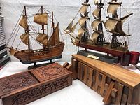 Photo showing two wooden ship models and two wooden decor boxes on a white cloth background.