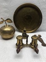 Wide view of the entire lot showing the round hammered brass tray, apple-shaped container, figurine, wall hanging, and salt and pepper shakers with stand.