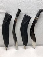 Full view of two Kukri knives with sheaths, showing curved blades and black leather sheaths with straps.