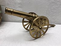 Side view showing full length and spoked wheels of solid brass toy cannon.