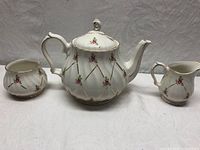 Front view of the teapot, sugar bowl, and milk jug showing swirl pattern and pink rose/gilt decoration.
