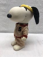 Side view of the vintage Snoopy doll showing the PVC head, fabric ears, and beige jogger outfit with 'S' patch and yellow visor.