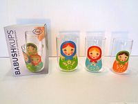 Set of three Babushkups by Fred drinking glasses with three colorful nesting doll designs alongside the original box.