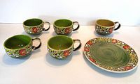 Five ceramic cups with green interiors and floral patterned exterior paired with a matching plate with similar floral border design.