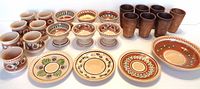 Overview of entire pottery lot showing decorated glazed bowls, plates, and small pots in front, and 7 tall un-glazed cups behind.