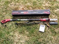Full view of electric pole saw extended next to original box and instructions on grass.