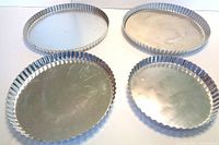Set of four fluted metal flan pans with removable bottoms, showing top view with some scratches and marks.