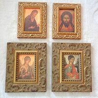 Four framed religious icon prints arranged on a surface, showing two smaller gold ornate frames with icon portraits on top and two larger thick antique style frames with angel icons below.