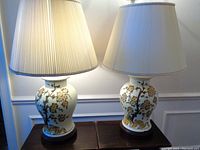 Pair of ceramic table lamps with beige pleated lampshades showing foliage and flower design, front view