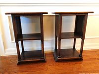Two matching wooden tables side by side against a wall, showing front view with two open shelves each.