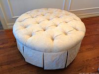 Round tufted ottoman stool showing top and pleated skirted base from front angle