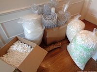 Overall view of boxes containing various packing supplies like bubble wrap rolls and packing peanuts bags.