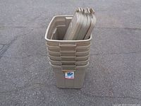 Six brown Rubbermaid storage totes stacked with lids placed on top, shown on asphalt ground.