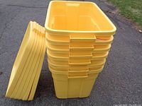 Stack of 6 yellow Rubbermaid storage totes with lids placed on the ground, showing size and shape.