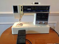 Front view of white Singer sewing machine with foot pedal and power cord visible