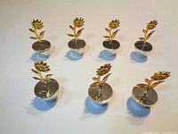 Top view showing eight golden sunflower place card holders in two rows, displaying detailed petals, leaves, and silver plated round bases.