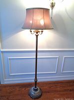 Full height view of the vintage floor lamp lit, showing bell-shaped fabric shade, slender pole, and round marble base on hardwood floor.
