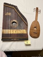 Photo showing both antique instruments on a white cloth: a chord zither and a smaller stringed instrument.