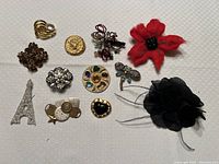 Collection of 13 assorted brooches including fabric flowers, rhinestone Eiffel Tower, and various gem and metal designs.