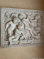 Front view of the rectangular white resin plaque showing four cherubs in relief with visible surface cracks.