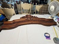 Full view of the wooden wall hanging laid on a table, showing the curved shape and detailed carvings with a broken top section.