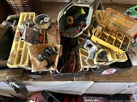 Fishing tackle box open showing reels, organizer box with sinkers and hooks, spools of line and fishing lures.