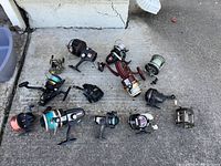 Full assortment of fishing reels with visible brand names and line colors on concrete ground outside.